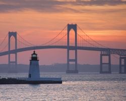 A lighthouse in front of the Claiborne Pell Bridge at sunset.