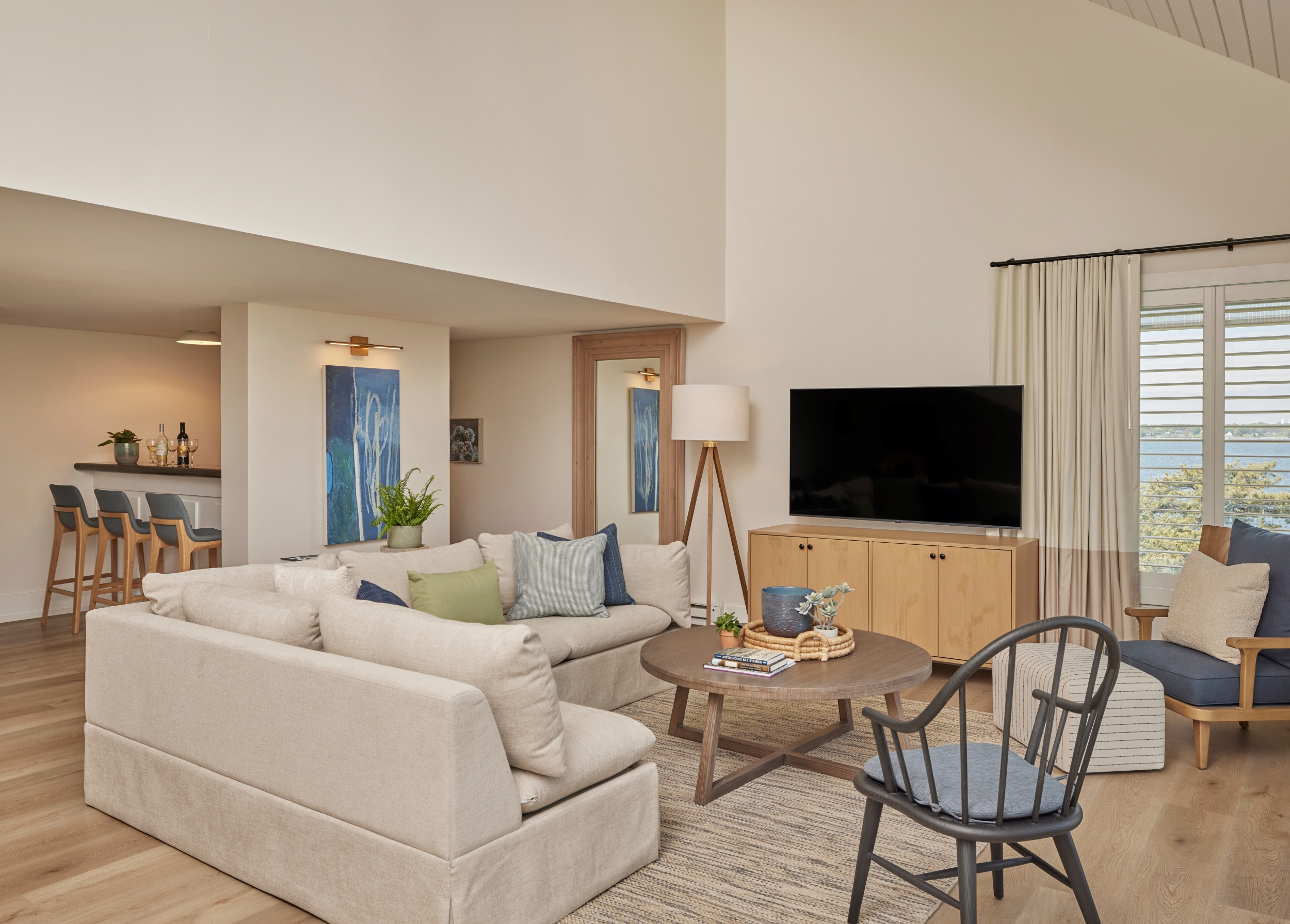 A spacious living room with a sectional sofa, coffee table, TV, and bar with stools.