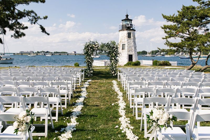 A seaside wedding aisle leading to a flower archway and a lighthouse.