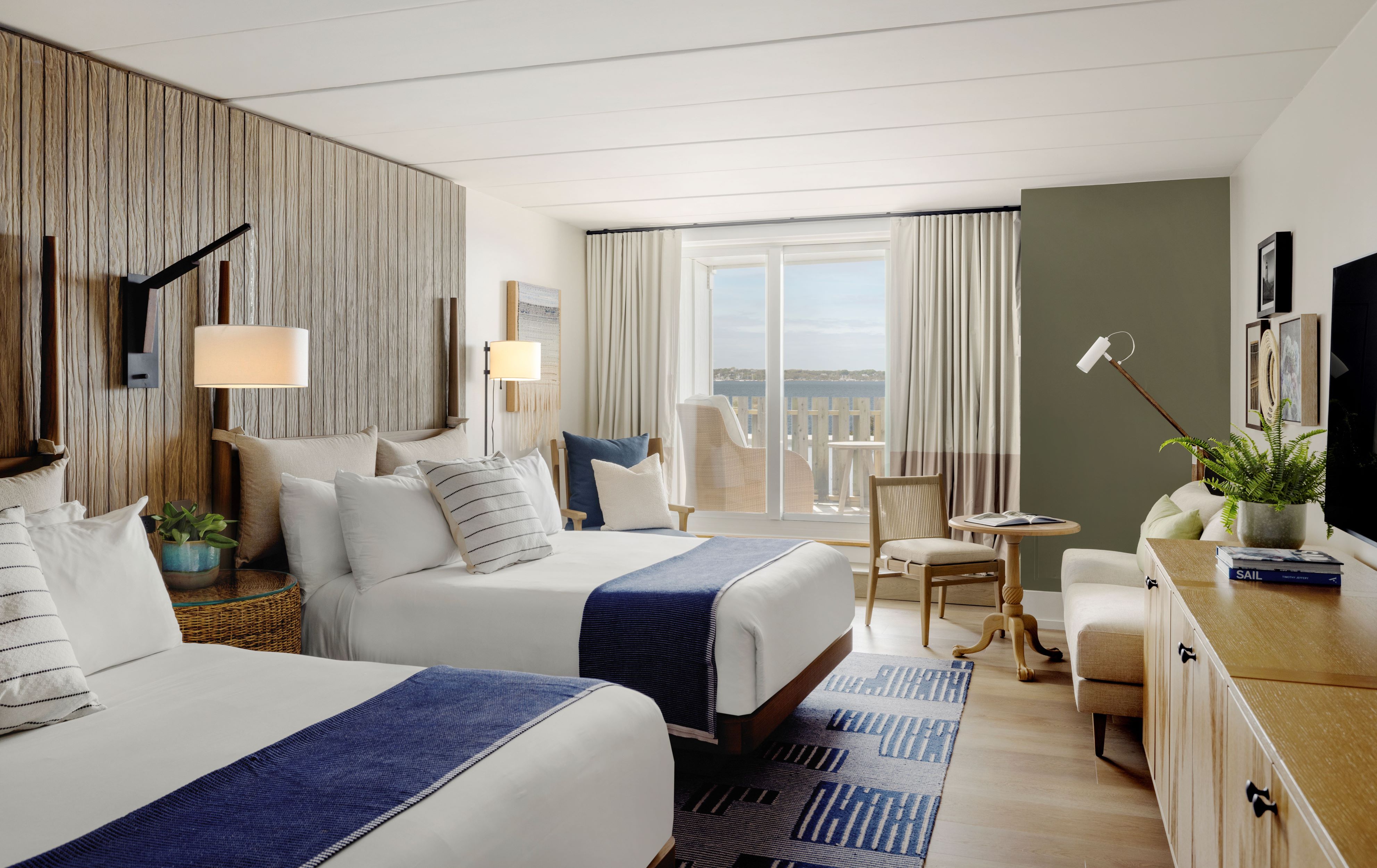 A hotel room with two beds, a desk, and a balcony with a water view.