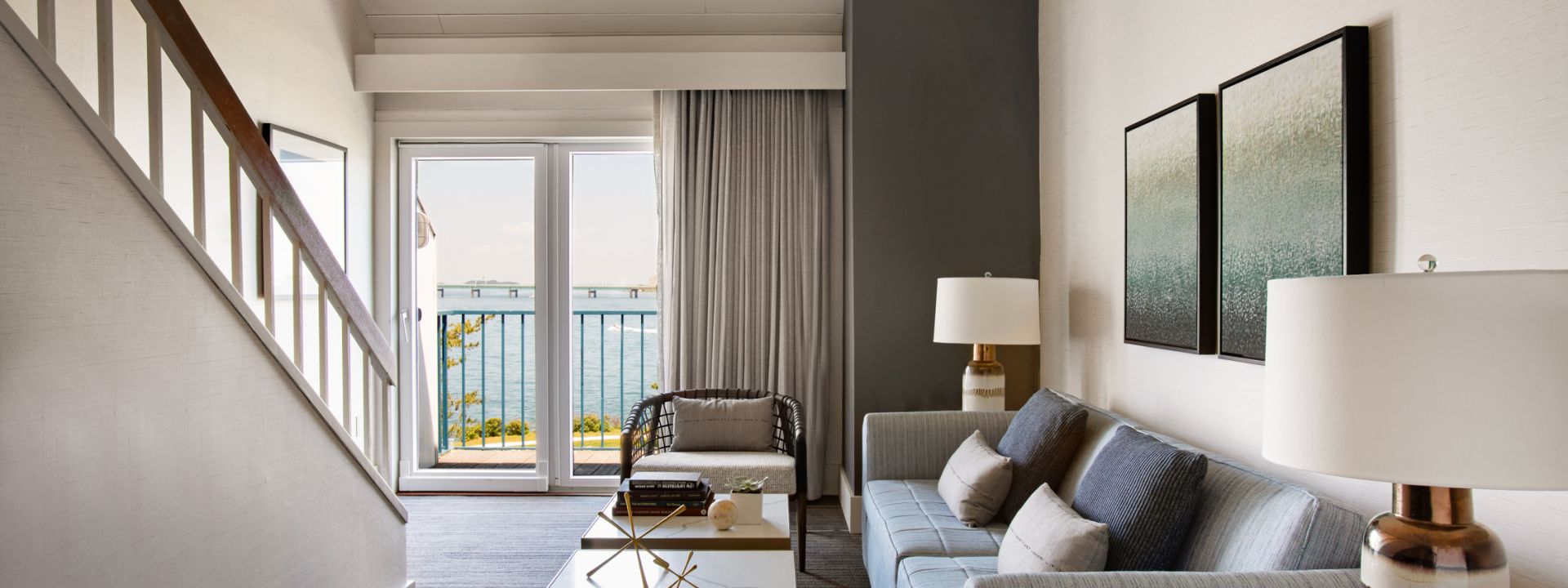 The living area of a bi-level hotel suite with a balcony and ocean views.