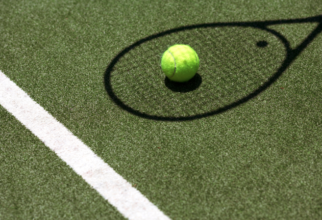 A tennis ball on astro turf inside the shadow of a tennis racket.