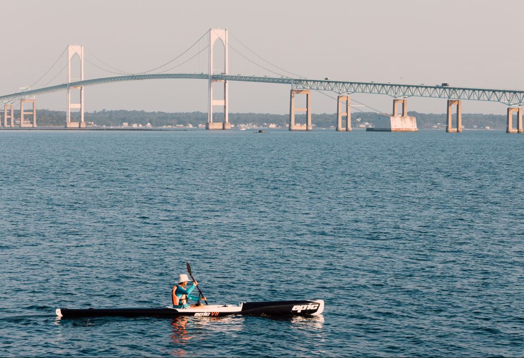 A person kayaking in the water with a large bridge in the background