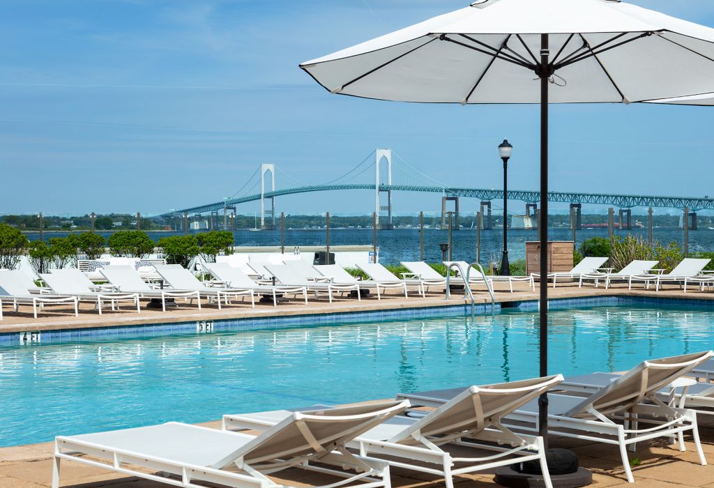 A pool with white lounge chairs and umbrellas, with a bridge in the background.