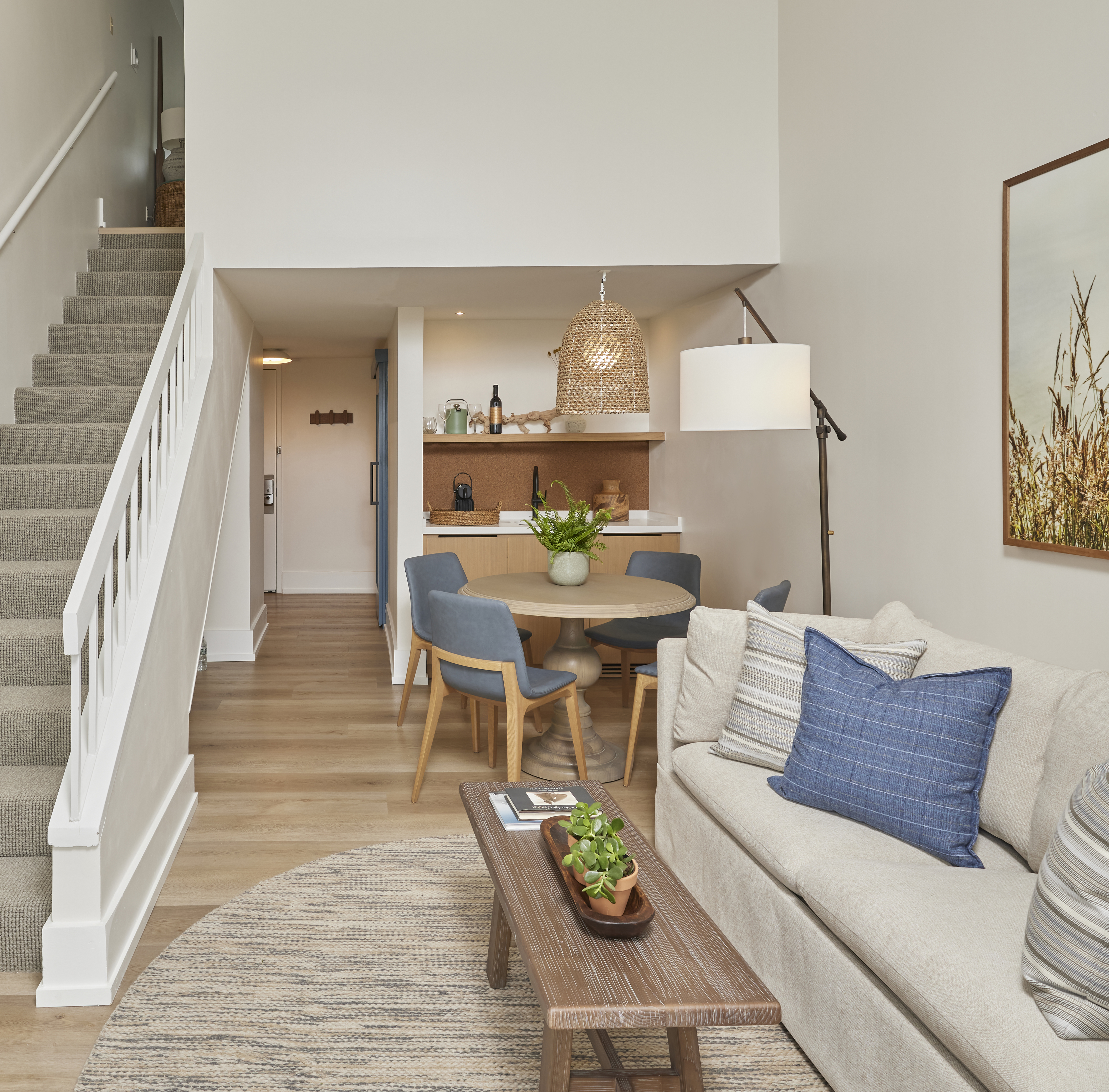 A wide view of a living area with a staircase, sofa, coffee table, dining table, and kitchenette.