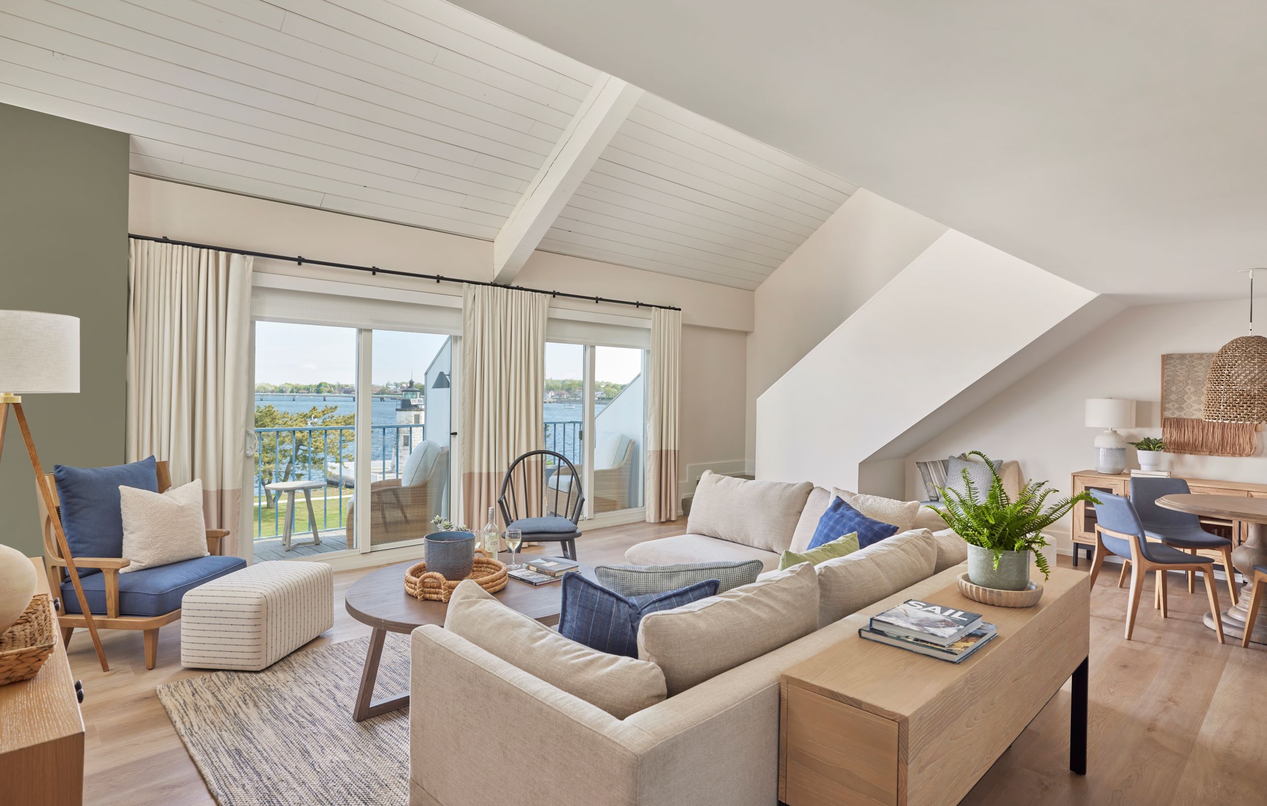 A living room with a beige sofa, coffee table, and chair, with a balcony visible through the window.