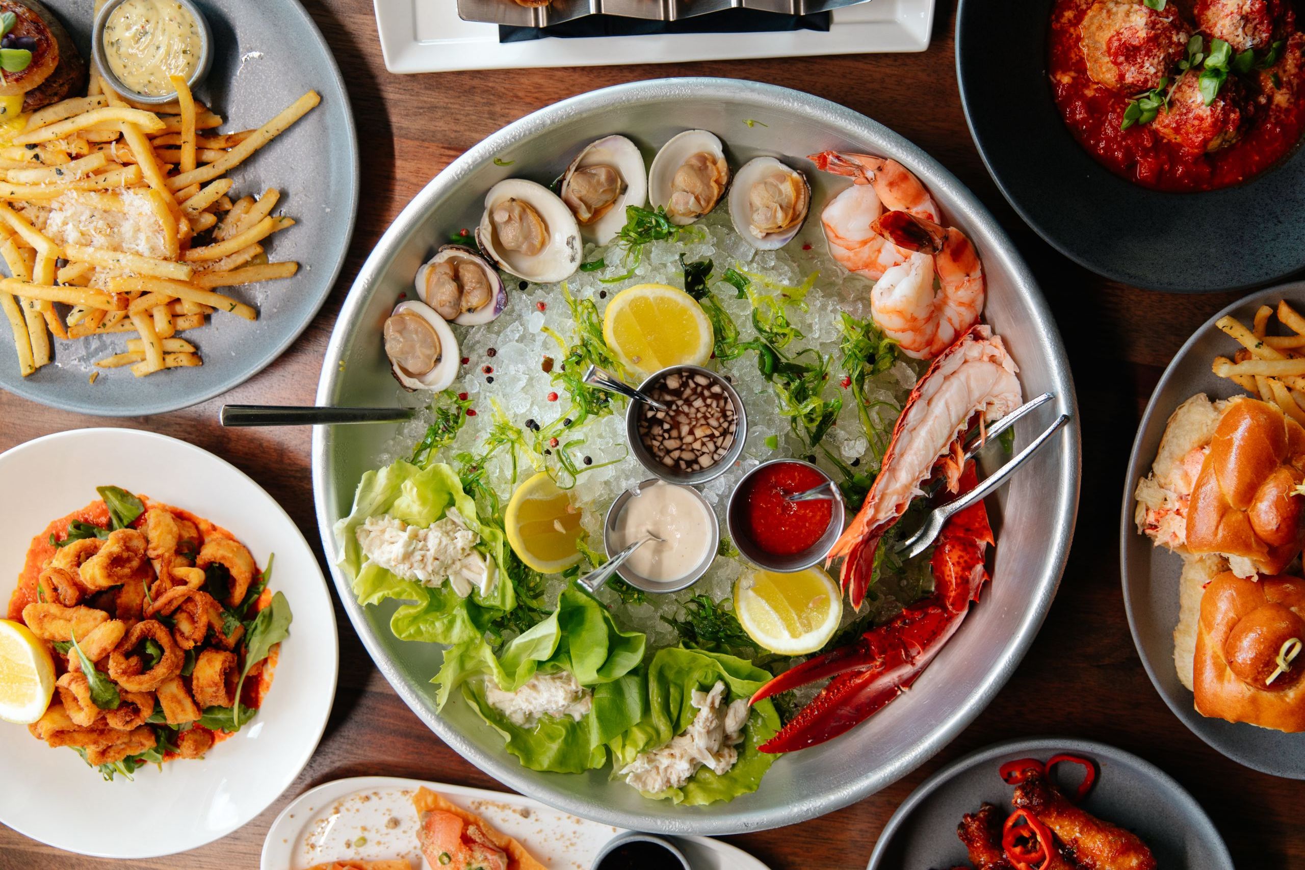 A large platter of seafood on ice with various sauces and lemon slices.