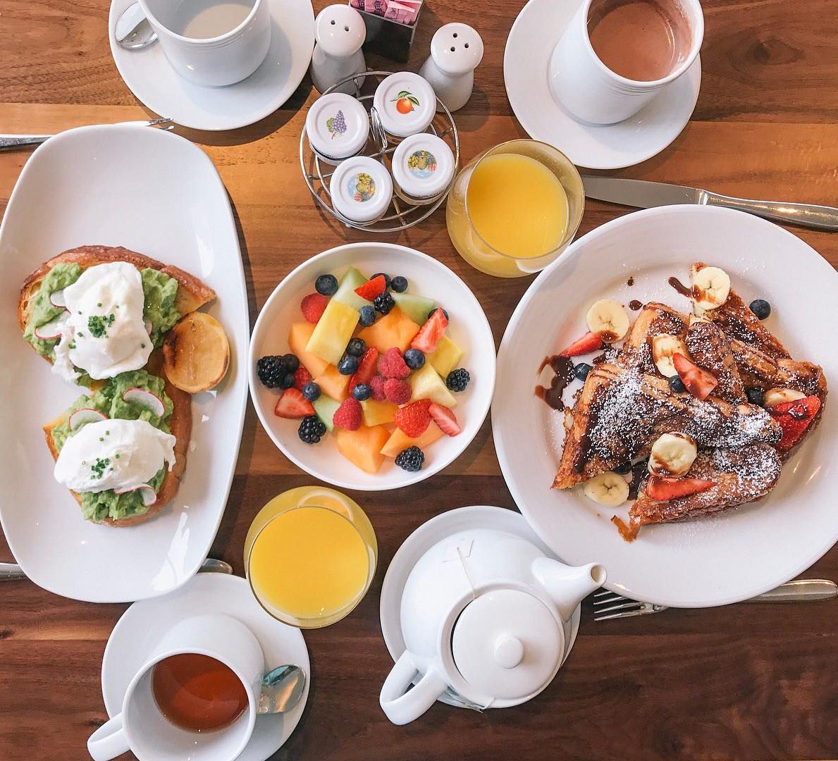 A breakfast spread with toast, fruit, and drinks on a wooden table.